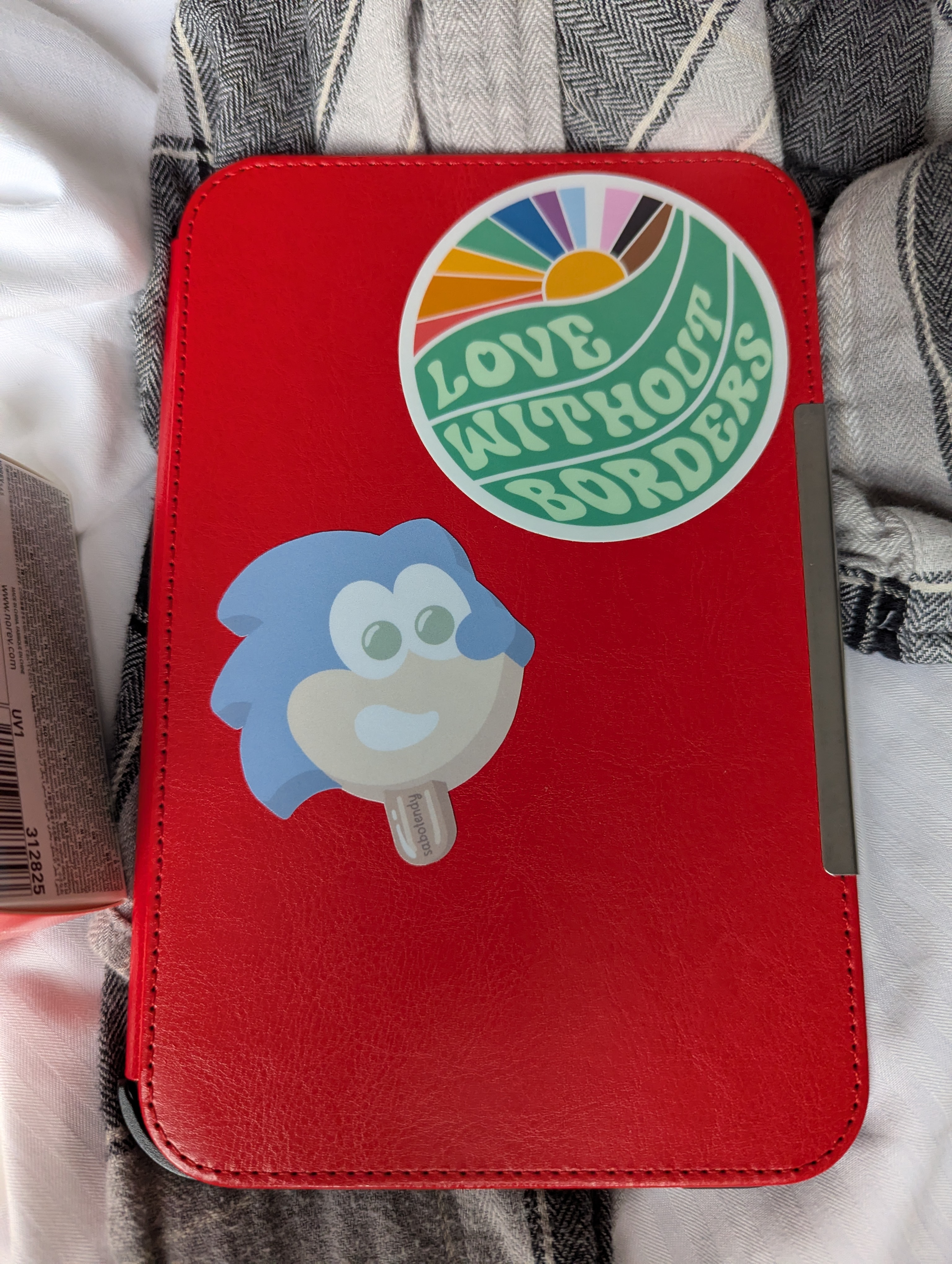 ereader in a red cover with two stickers on it: One that says "LOVE WITHOUT BORDERS" and another of Sonic the Hedgehog rendered as a ice cream truck-style popsicle
