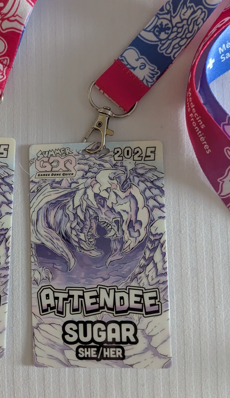 Cropped photo of one attendee badge for Summer Games Done Quick 2025, the other one is out of the image. It features a pastel purple and white dragon art. The text on the badge indicates my handle "sugar" and pronouns "she/her".  The lanyard is red and blue and features art from Final Fantasy 9.  I suspect the dragon is also from FF9