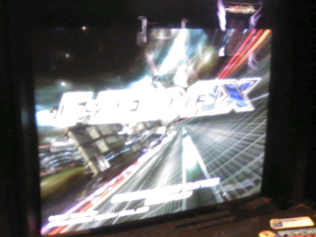 Super blurry photograph of one of the F-Zero AX arcade cabinets.  Close up on the title screen on the monitor.