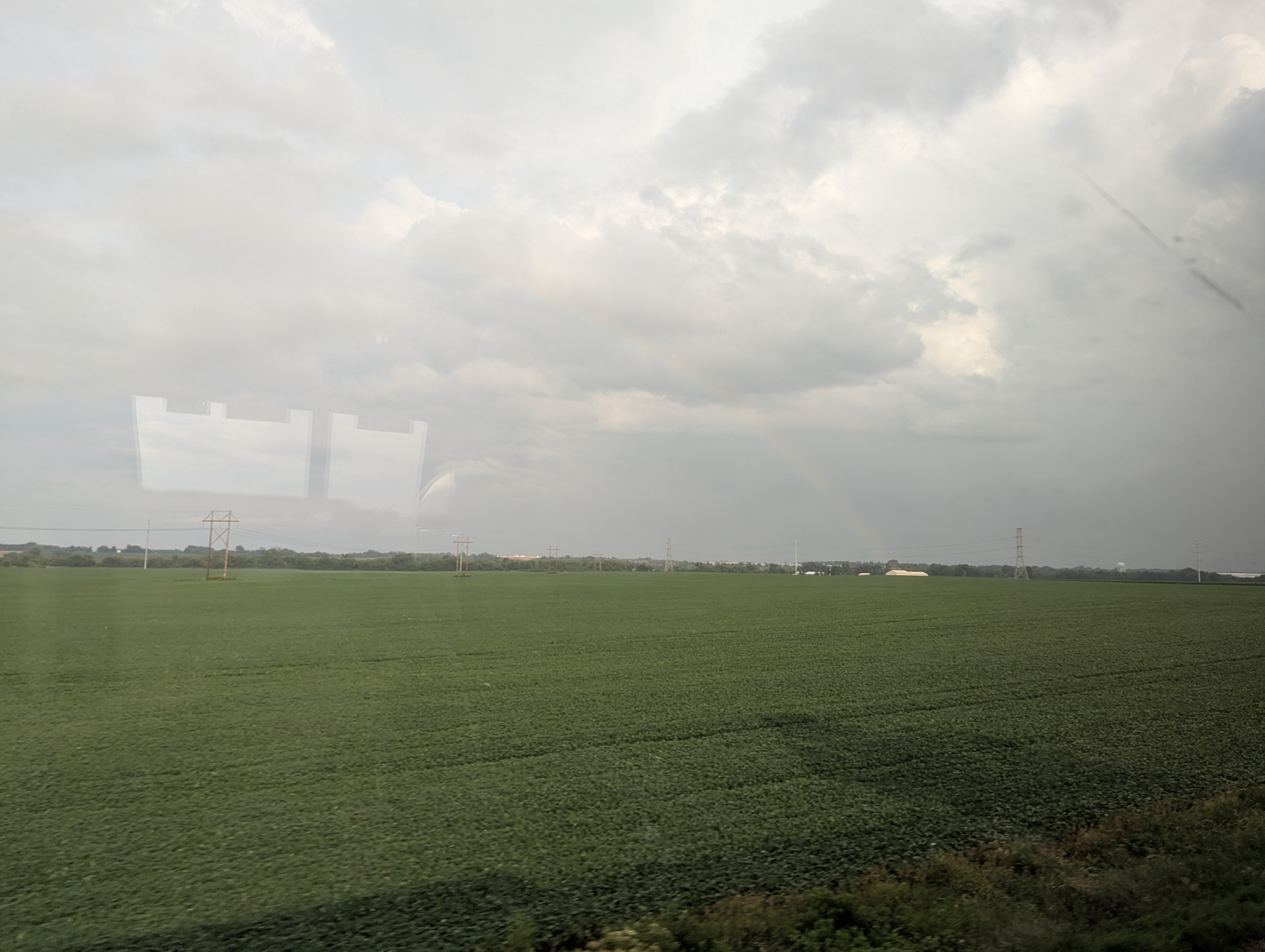 Photograph of a large open green farm field with dark storm clouds.