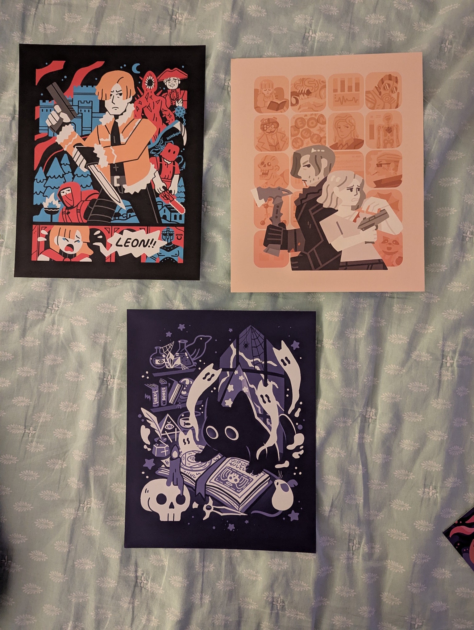 The posters I picked up from Artist's Alley.  They're all very stylized with few colors.  The first one is for _Resident Evil 4_ and features Leon, Ashley, the chainsaw man, Salazar, the shop keep, and RE4's version of the Tyrant.  The scenery shows trees, village houses, and the big castle.  The primary colors are blue and red, with orange highlighting Leon's jacket and hair as well as Ashley's hair.  The second print is for RE9 featuring characters and scenes from the game (that I haven't reached yet so don't know how to describe) as the background while Leon and Grace are in front.  The background is orange and orange tints while Leon and Grace are largely grey and black.  The third print is black, purple, and white, showing a black cat studying a spellbook surrounded by objects of the occult.  White ghost cats are dissipating upwards from the book.