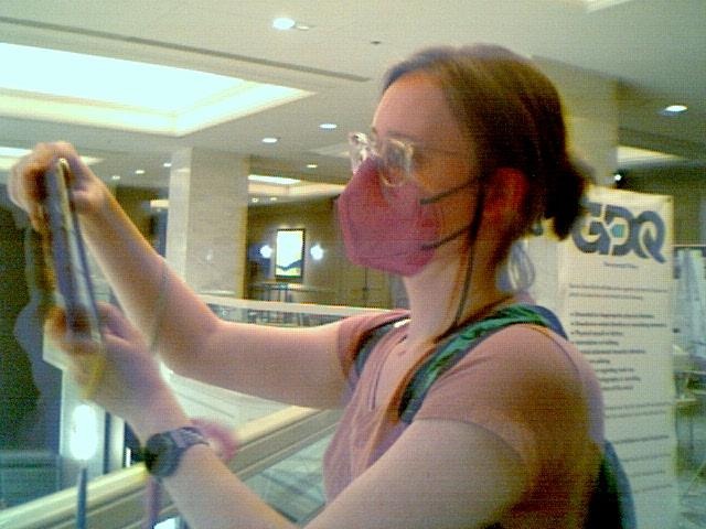 photograph of me taking a photograph of the previous chandelier using my 3ds.  I am in a pink top with a pink KN95 mask.  you can see I'm on the mezzanine at the edge of the railing.  behind me is a sign that says GDQ with a bunch of smaller text below it.