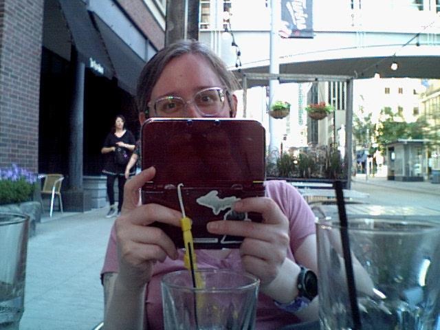 Photograph of me holding my 3DS taking a picture of my wife.  My face  below my eyes is hidden behind the 3DS, but my eyes are clearly smiling.